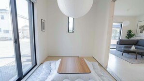 Ein Zimmer mit einem Bett, einer Schiebetür, einem kleinen Fenster, einem grauen Sofa und einer weißen Pendelleuchte.