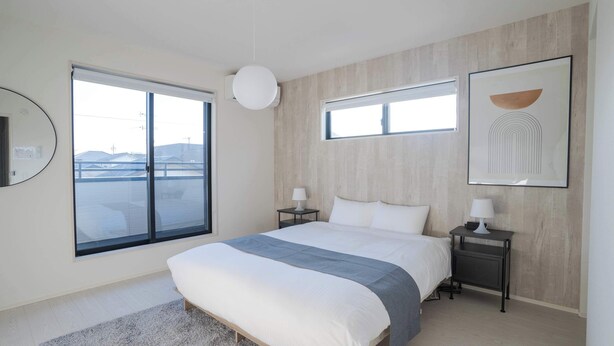 Ein modernes Schlafzimmer mit einem großen Bett, zwei Nachttischen mit Lampen, einem großen Fenster mit Jalousien und einem gerahmten Kunstwerk an der Wand.