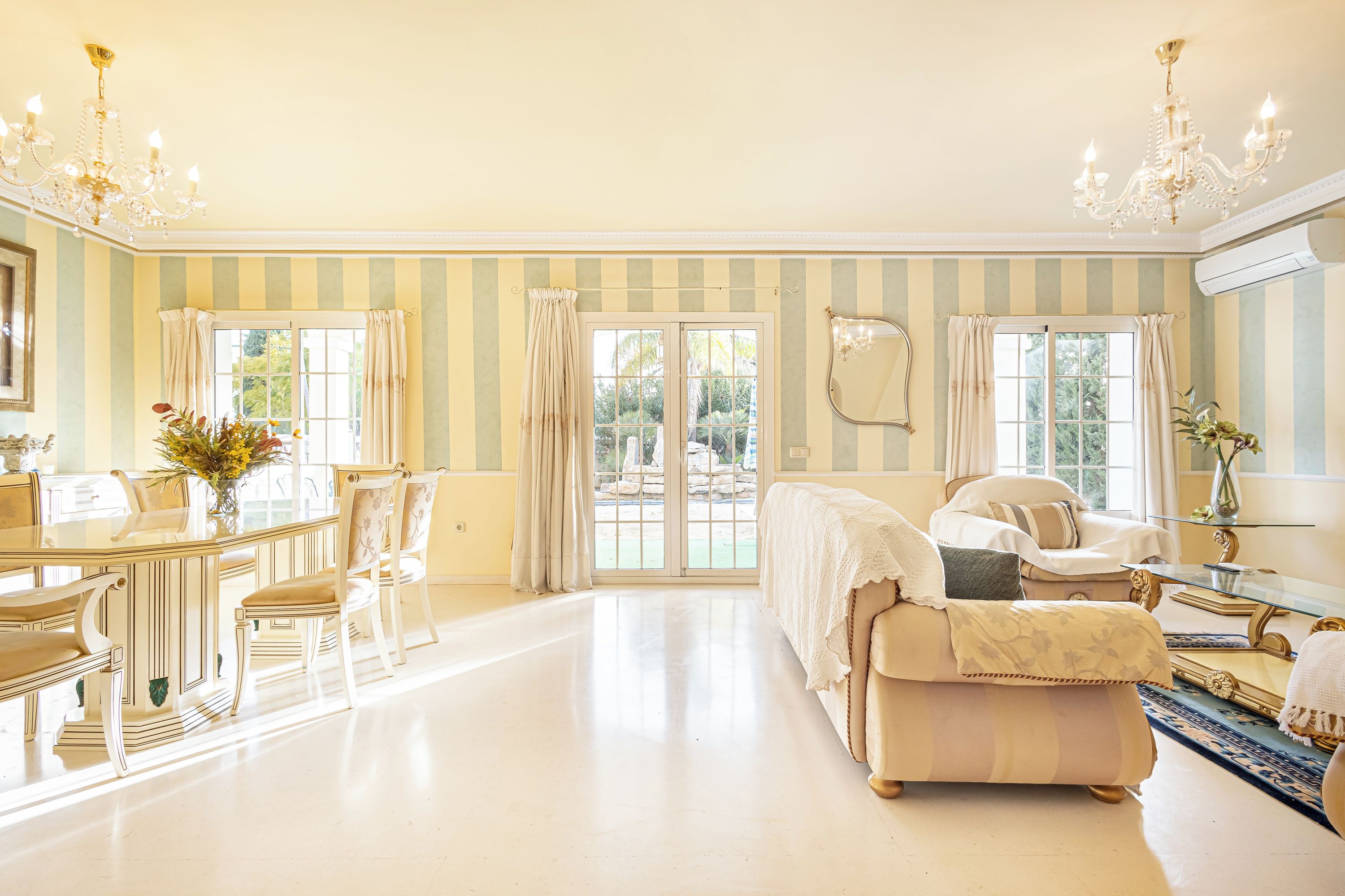A spacious room with a dining table, chairs, a sofa, and a large window with curtains.