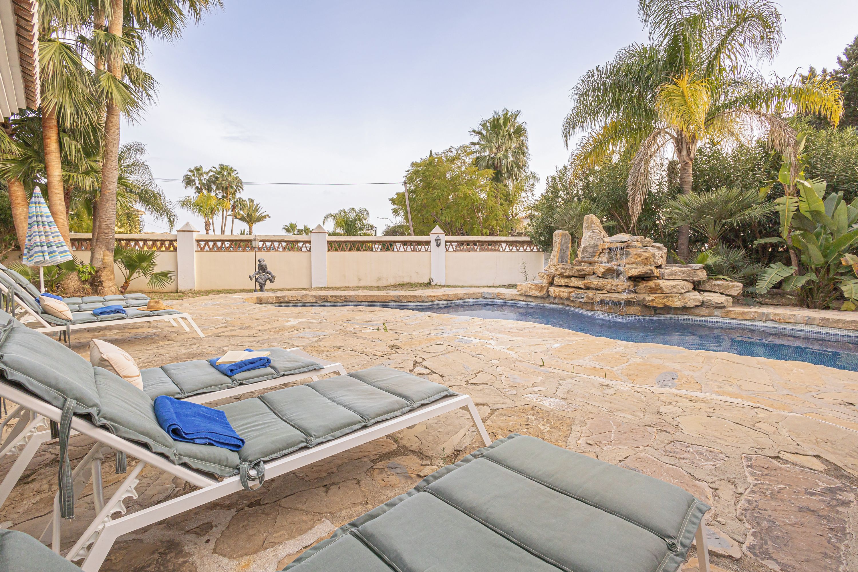 A poolside area with lounge chairs, a stone-tiled deck, and a stone wall with a decorative top.