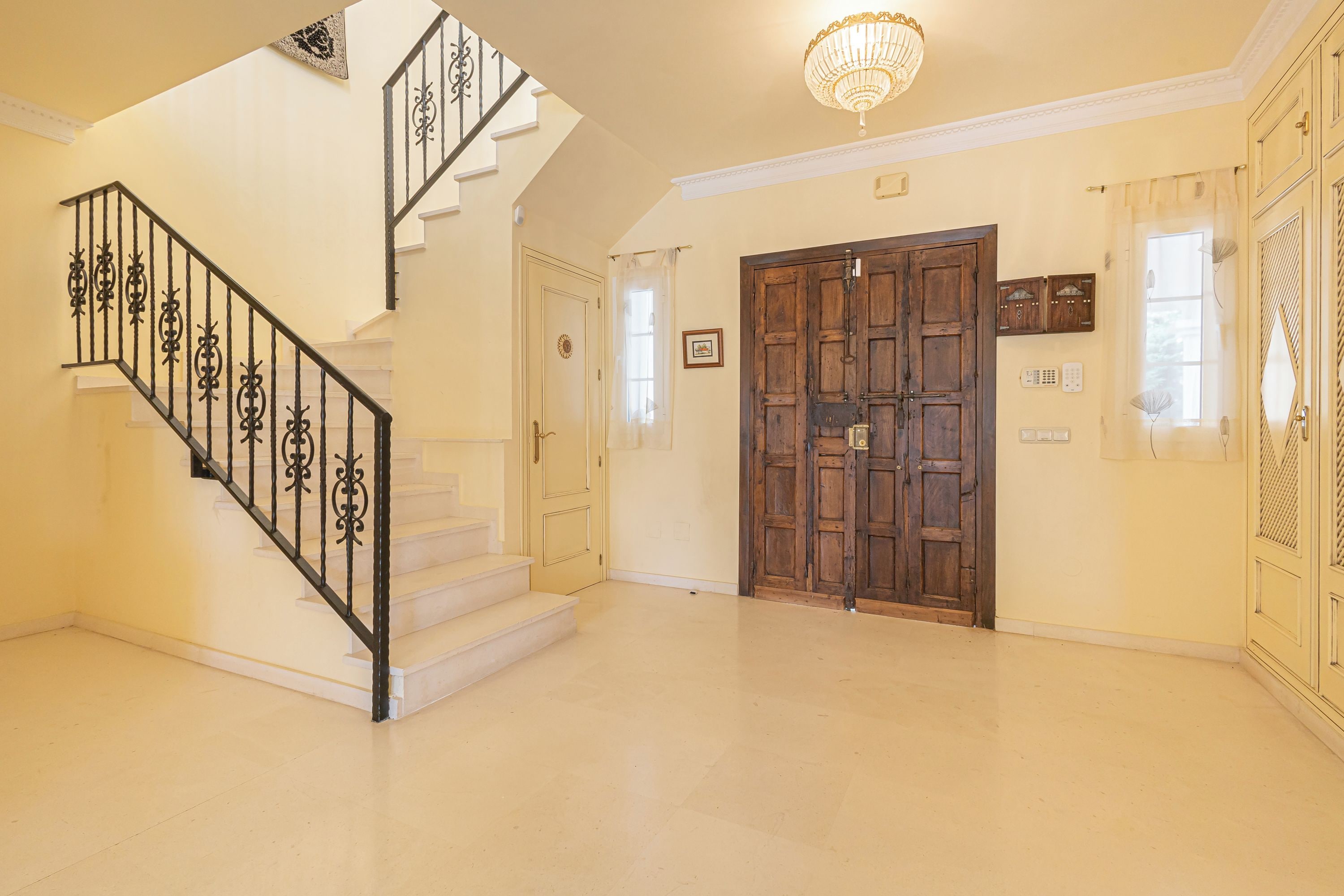A staircase with ornate metal railings, a chandelier, and a large wooden door.