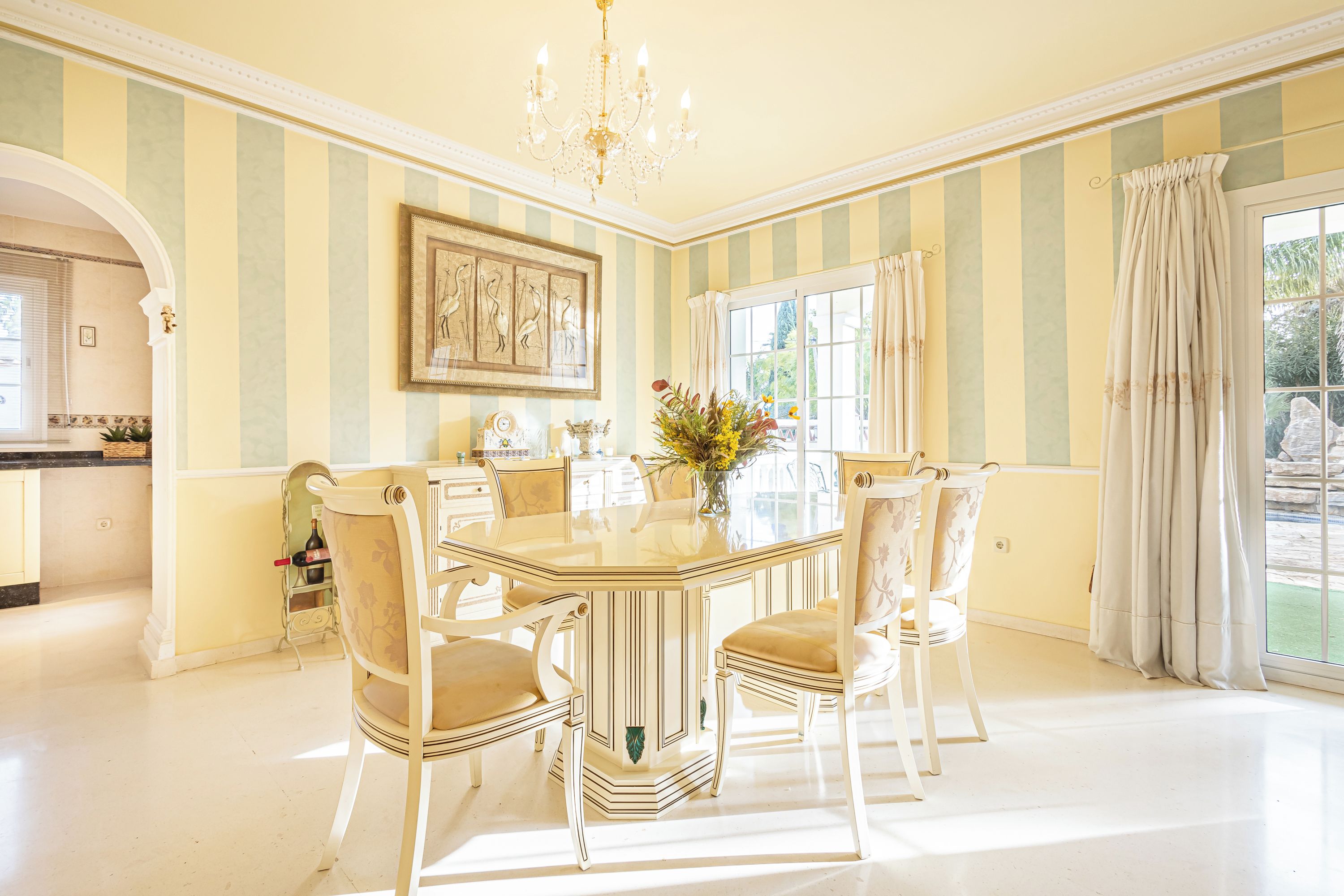 A dining room with a glass table, striped wallpaper, and a chandelier.