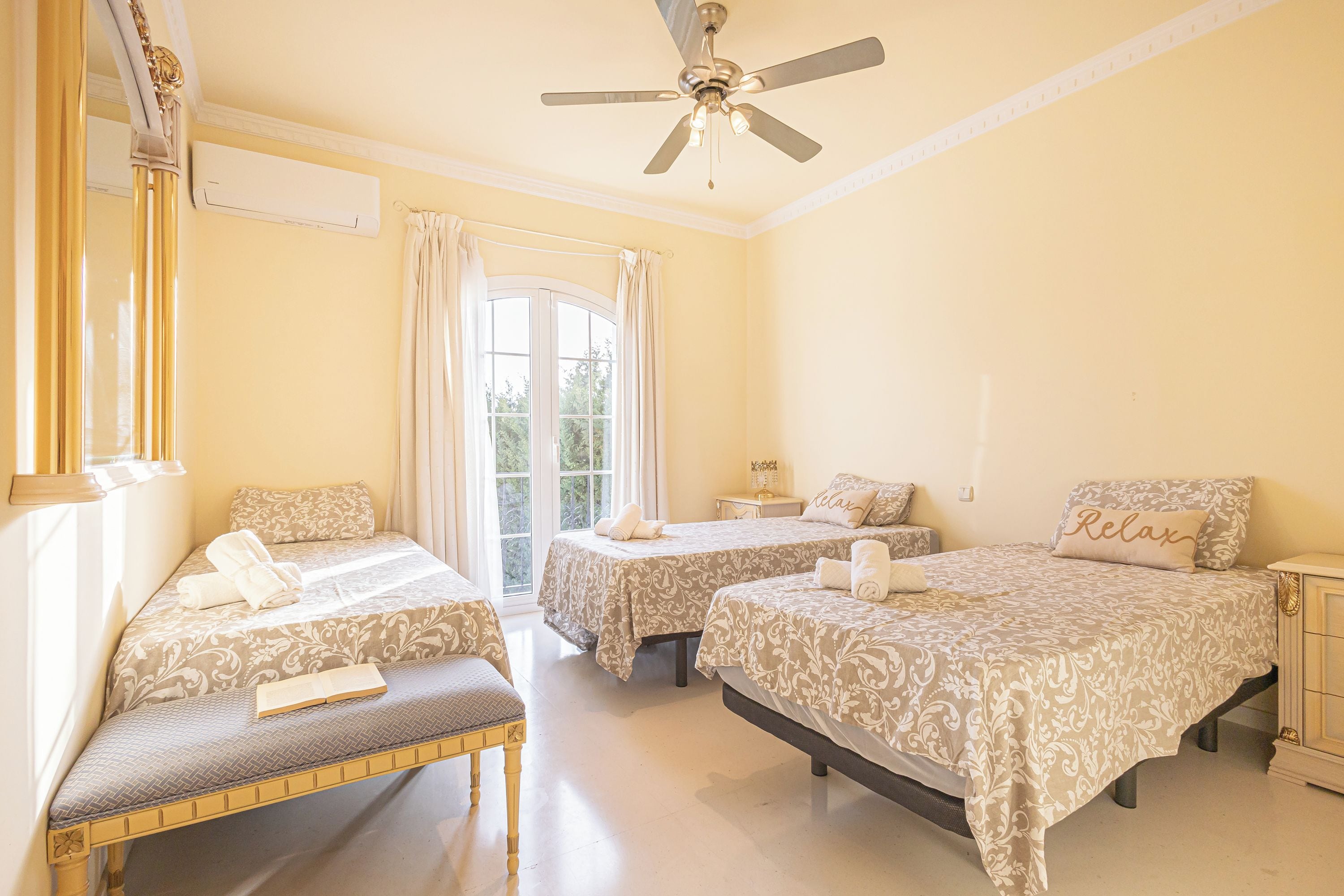 A hotel room with two beds, a bench, a ceiling fan, and a window with curtains.