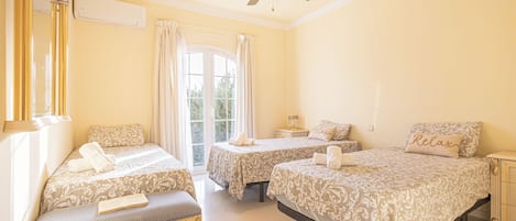 Une chambre d’hôtel avec deux lits, un banc, un ventilateur de plafond et une fenêtre avec des rideaux.