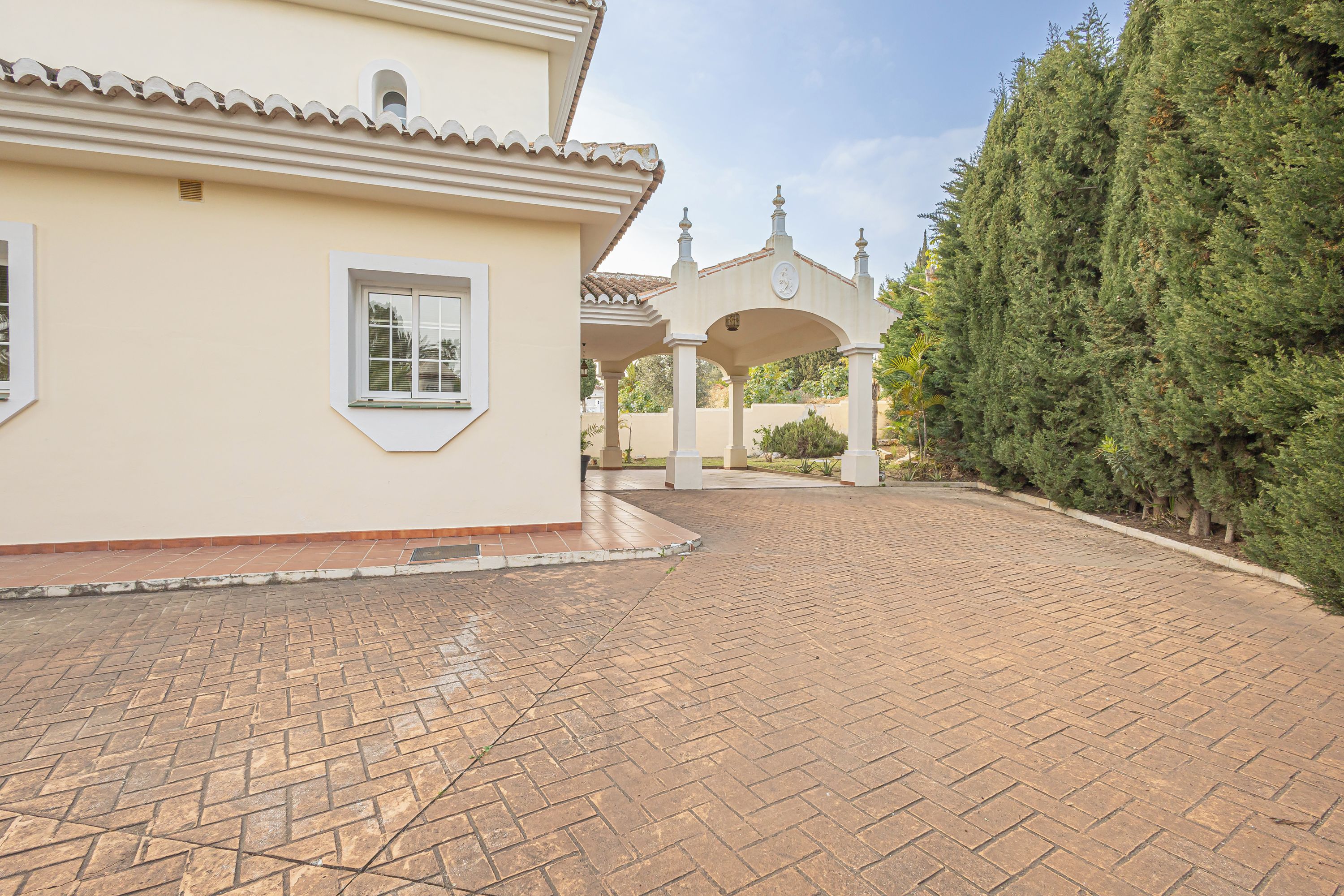 A paved driveway leading to a building with a tiled roof and a covered entrance.