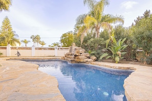 A swimming pool with a stone border, surrounded by tropical plants and a decorative rock feature. - Family Villa for 7 Mijas Golf With Pool (Mijas)