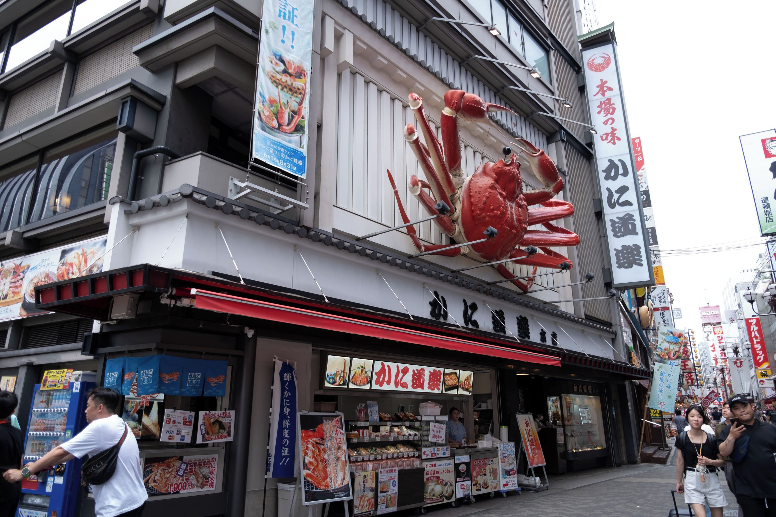 A building with a large crab decoration on the facade, a sign with Japanese characters, and a storefront with various items displayed outside.