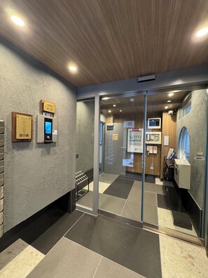 A reception area with a digital display, a plaque, and a glass door leading to a room. - The Peak Shinsaibashi Elite (Osaka)