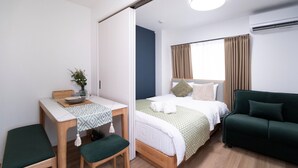 Een kamer met een bed, een groene bank, een bureau met stoel en een kleine tafel met een vaas.