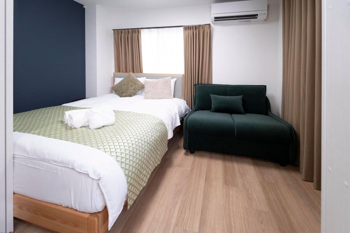 Ein Hotelzimmer mit Bett, Sofa, Vorhängen an einem Fenster und einer Klimaanlage.