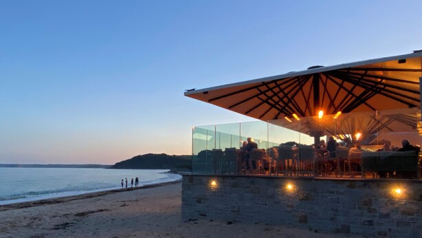 Un ristorante sulla spiaggia con un'area vetrata, pareti in pietra e vista sul mare.