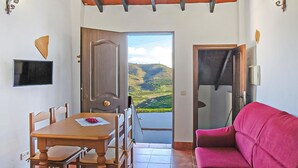 Una habitación con una mesa de comedor, sillas, un sofá rosa y vistas a un paisaje montañoso a través de una puerta.