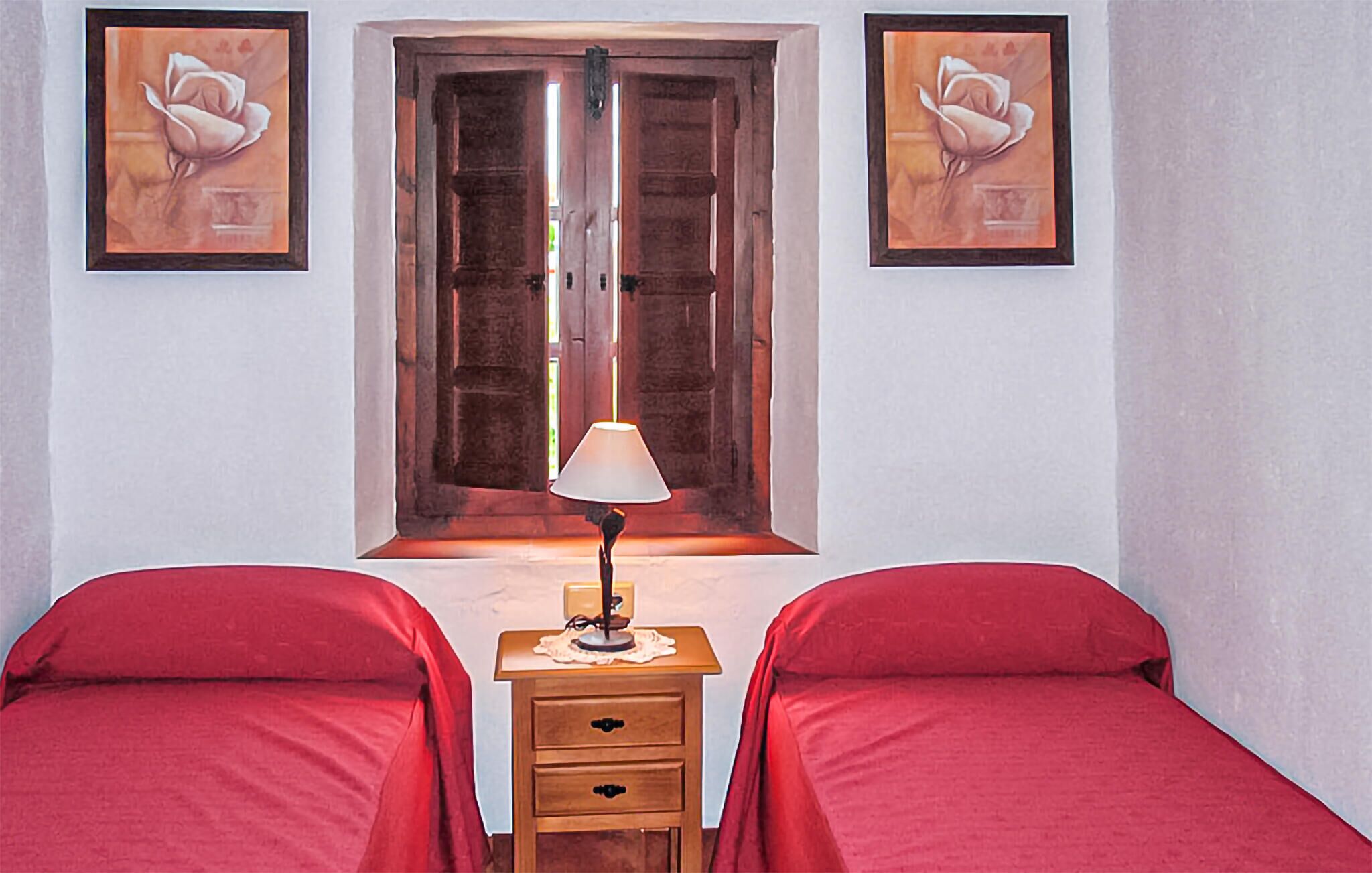 Quarto com duas camas, uma mesa de cabeceira, uma luminária e duas fotos emolduradas na parede.