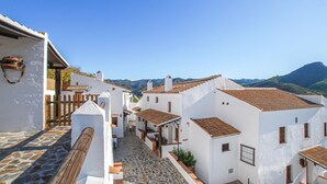 Una calle estrecha con edificios blancos, pavimento de piedra y montañas al fondo.