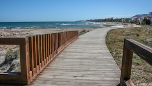 A wooden boardwalk leading to a beach with a clear view of the ocean and distant buildings. - Stunning apartment in Cabanes with swimming pool (Cabanes)