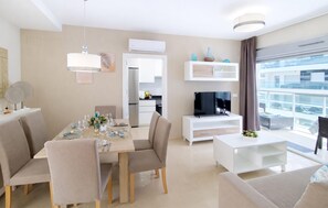 Ein modernes Wohnzimmer mit Essbereich, Fernseher und einem Balkon mit Blick auf die Stadt.
