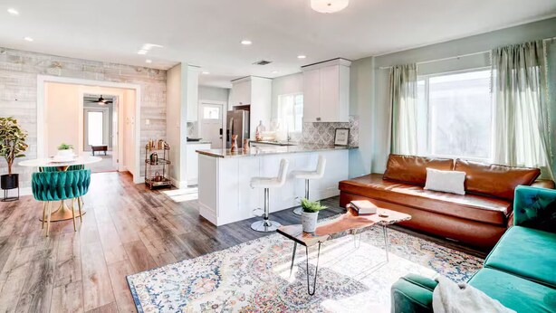 A modern living room with a sofa, a dining area with a table and chairs, a kitchen area, and a large window with curtains. - The Montecito Midpoint — spacious — 100" TV (Phoenix)