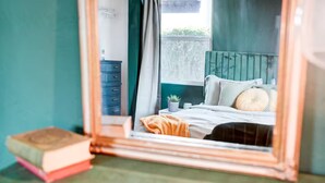 A bedroom with a bed, pillows, a bedside table, a small plant, and a mirror reflecting the room. - The Montecito Midpoint — spacious — 100" TV (Phoenix)