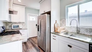 A modern kitchen with white cabinetry, a stainless steel refrigerator, a microwave, and a sink with a window above. - The Montecito Midpoint — spacious — 100" TV (Phoenix)