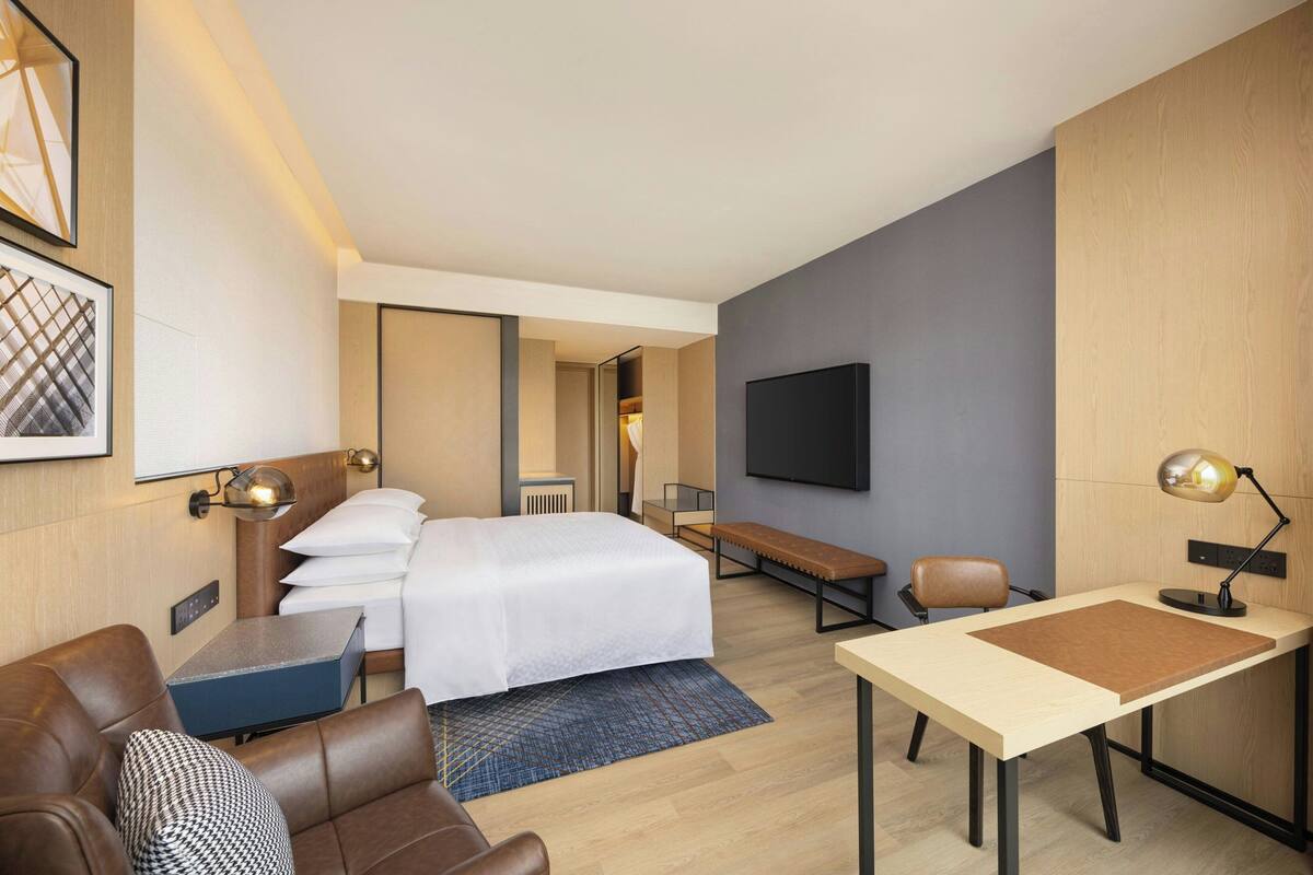 Una habitación de hotel moderna con una cama, un escritorio, una silla, un sofá, un televisor y un espejo.