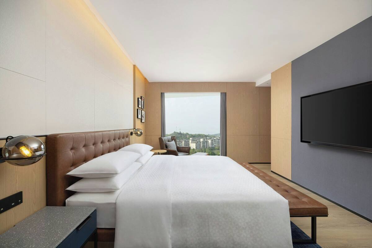 Una habitación de hotel moderna con una cama grande, un televisor de pantalla plana, vistas de la ciudad y un banco de madera.