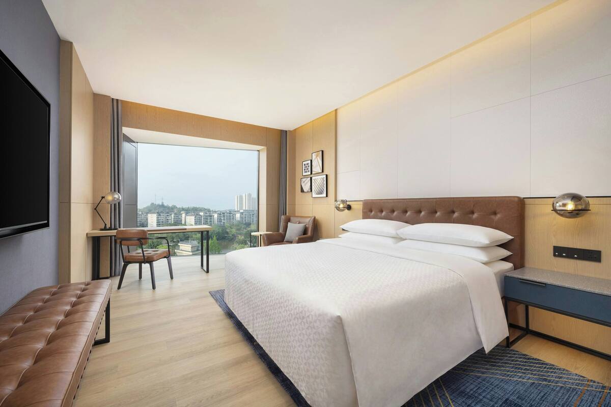 Una habitación de hotel moderna con una cama grande, un escritorio, una silla y vistas a la ciudad.