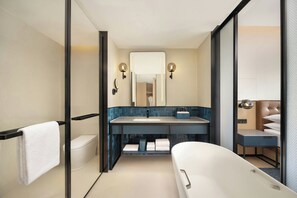 Een moderne badkamer met een douchecabine van glas, een witte badkuip, een grote spiegel en een blauw betegelde wastafel.