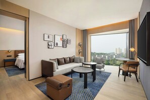 Ein modernes Hotelzimmer mit einer Couch, einem kleinen Tisch, einem Sessel, einem Bett und einem großen Fenster mit Blick auf die Stadt.