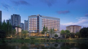 A modern hotel with a reflective pool, surrounded by greenery and other buildings.