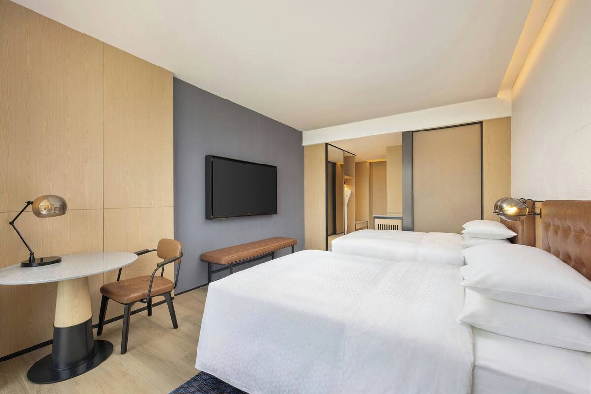 Una habitación de hotel con cama, escritorio, silla, televisor y espejo.