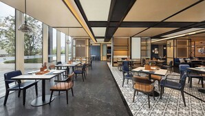 A modern dining area with tables and chairs, large windows, and a patterned floor.