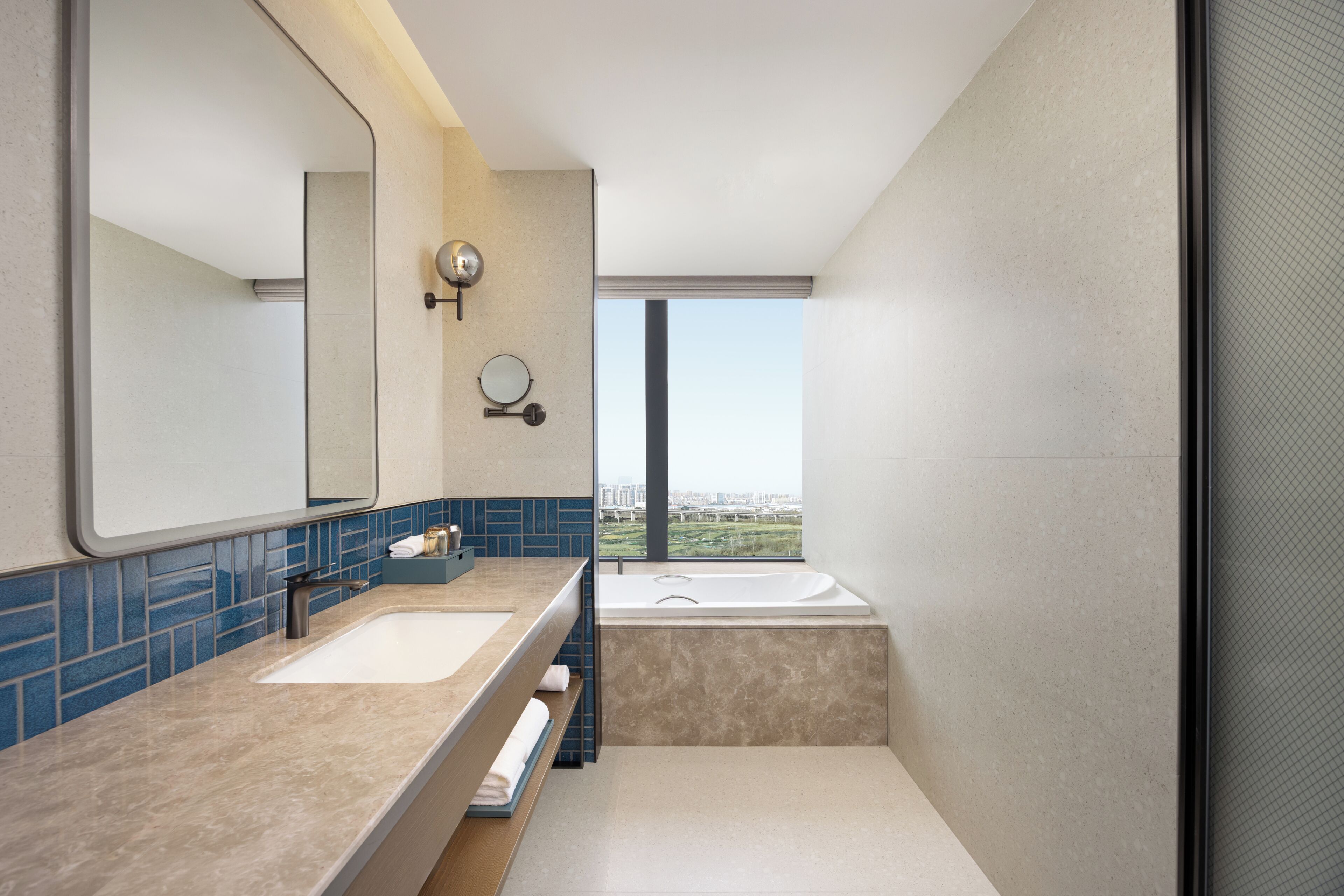 A modern bathroom with a large mirror, two sinks, a bathtub, and a view of the city.