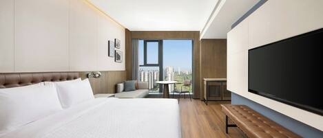 Habitación de hotel con una cama grande, zona de estar con una mesa, televisión y vistas a la ciudad.