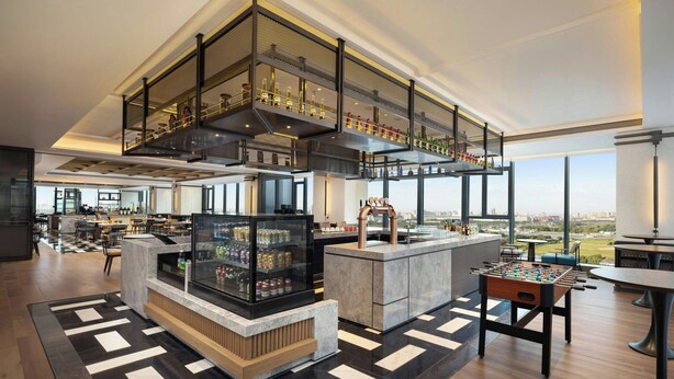 En moderne hotellobby med højt til loftet, et centralt barområde, et fodboldbord og et stort glasdisplay.