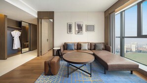 Et moderne hotelværelse med et stort vindue, en sofa, et rundt sofabord og et garderobeskab.