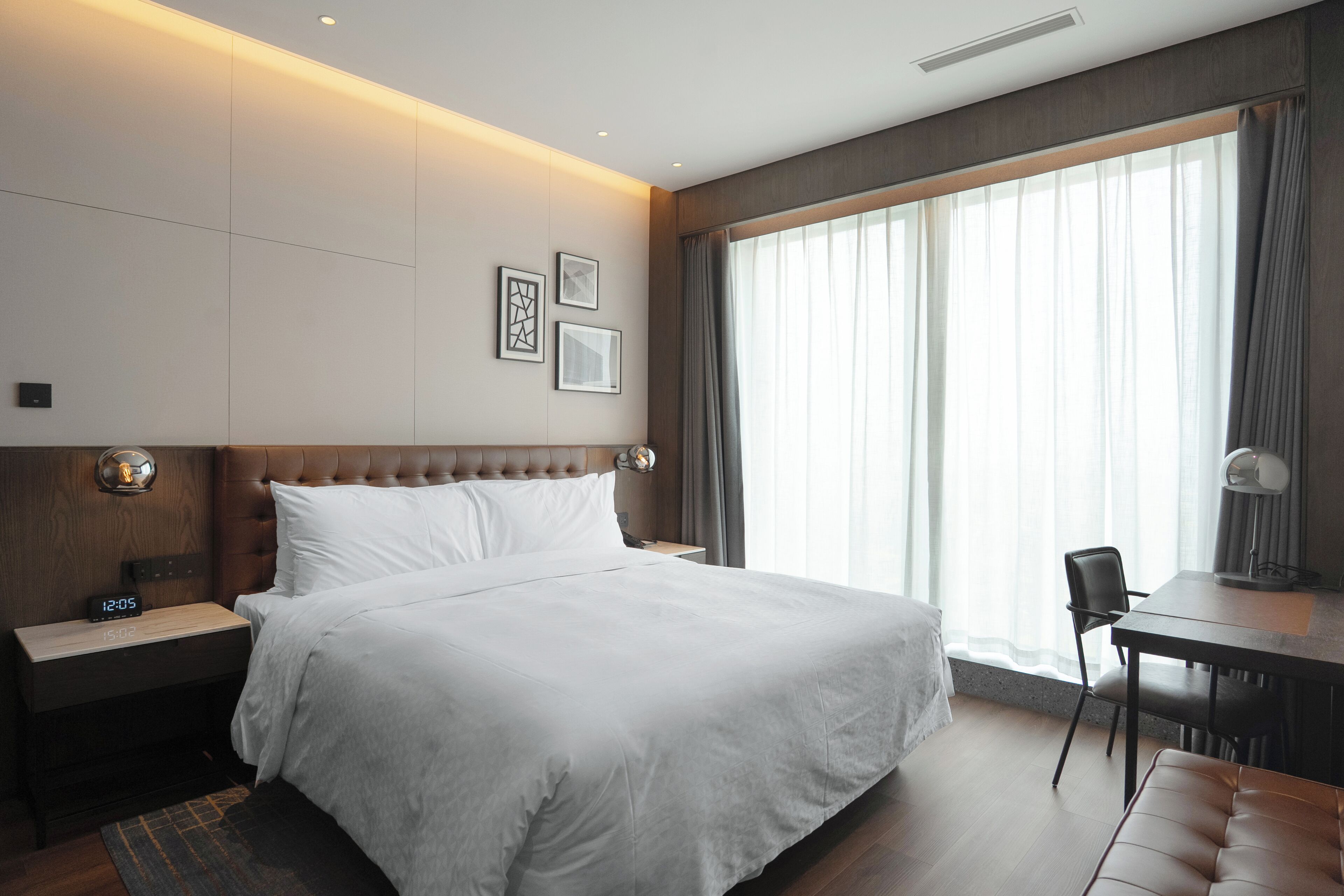 Una habitación de hotel moderna con una cama grande, un escritorio, una silla y un ventanal con cortinas.