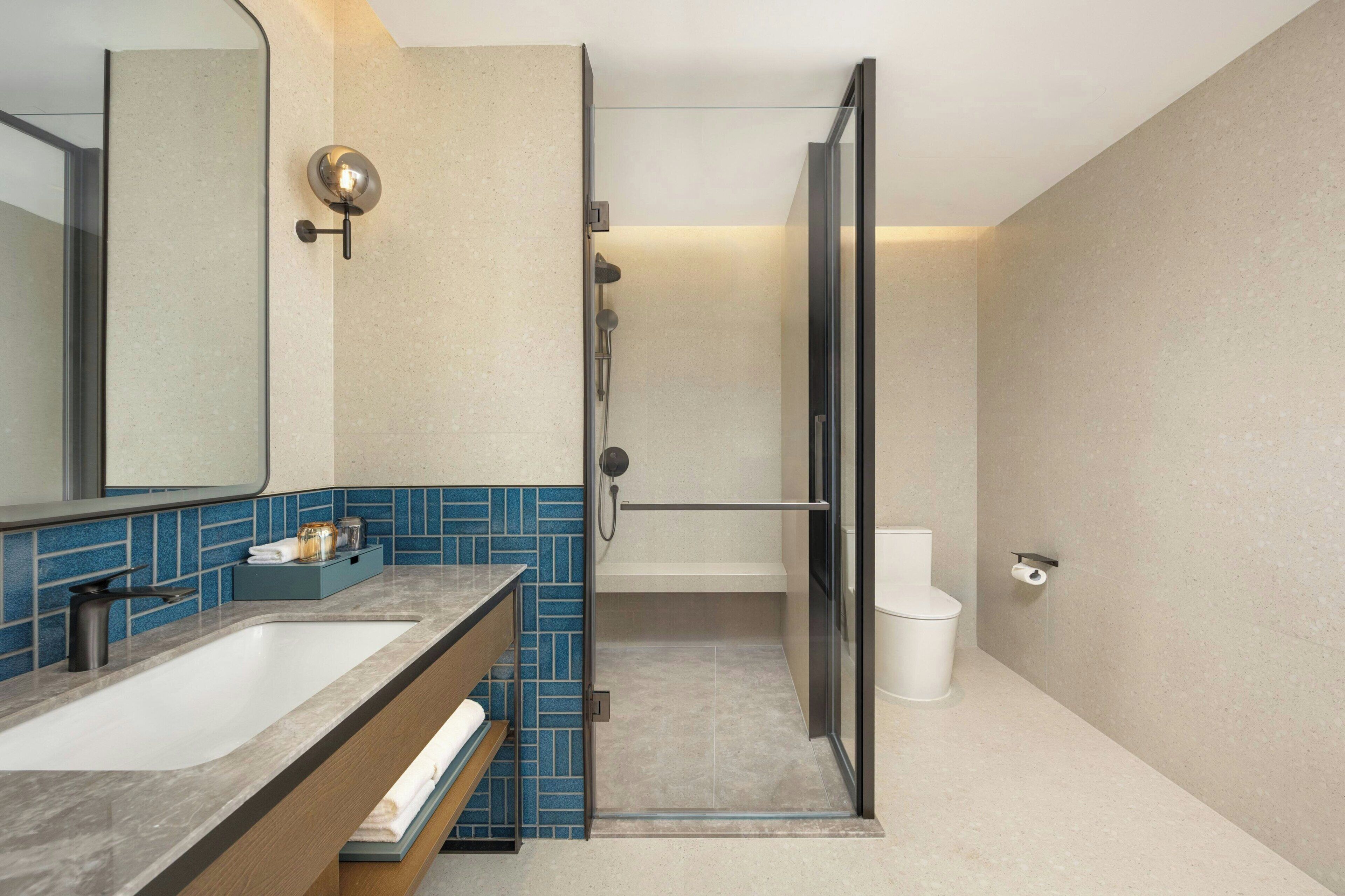 A modern bathroom with a large mirror, a sink, a shower, and a toilet.
