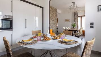 Zona pranzo con tavolo rotondo, sedie in vimini e cucina con pensili bianchi e forno a incasso.