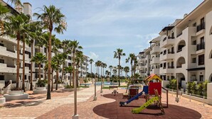 A children's playground with slides and swings, surrounded by palm trees and a pool. - Cozy apartment in Murcia (Murcia)
