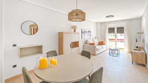 A modern living room with a round dining table, a sofa, and a coffee table. There is a large window with curtains, a ceiling light, and a wall-mounted mirror. - Cozy apartment in Murcia (Murcia)