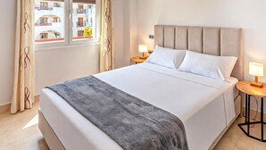 A neatly made bed with a grey throw, two bedside lamps, and a window with curtains. - Cozy apartment in Murcia (Murcia)