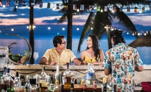 Zona de bar con temática tropical, con palmeras y vista al atardecer.