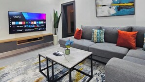 Moderni olohuone, jossa on litteänäyttöinen televisio, harmaa sohva värikkäillä koristetyynyillä, sohvapöytä maljakolla ja taulu seinällä.