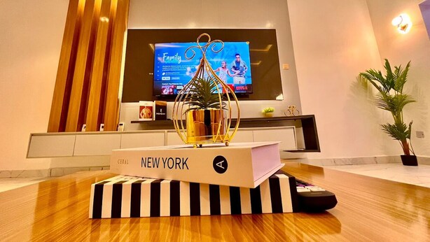 Moderni olohuone, jossa on litteänäyttöinen televisio, koristeellinen kasvi ja puupöydällä kirja, jonka nimi on ”NEW YORK”.