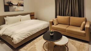 Moderni hotellihuone, jossa on sänky, sohva, pyöreä sohvapöytä ja taulu seinällä.