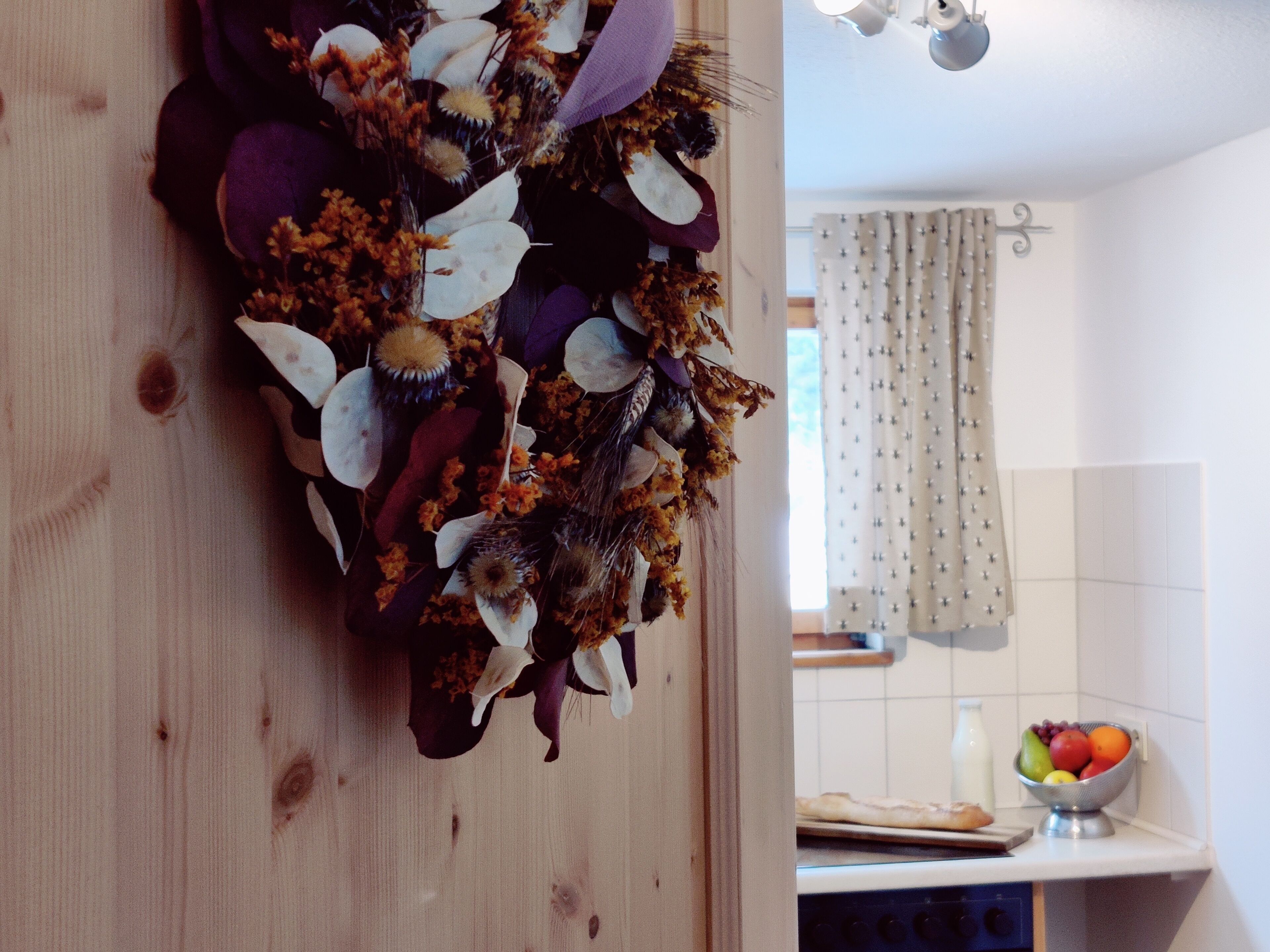Une cuisine avec un plan de travail en bois, un saladier rempli de fruits et une fenêtre avec des rideaux.
