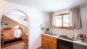 A compact kitchen with wooden cabinets, a built-in oven, and a window with curtains. - Between blossoms & mountains, welcome to the beehive (Fischen im Allgäu)