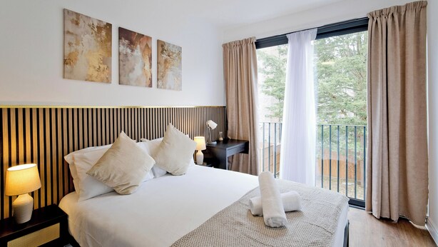 Een hotelkamer met een groot bed, een nachtkastje met een lamp, een bureau met een lamp, en uitzicht op de omgeving door een schuifdeur.