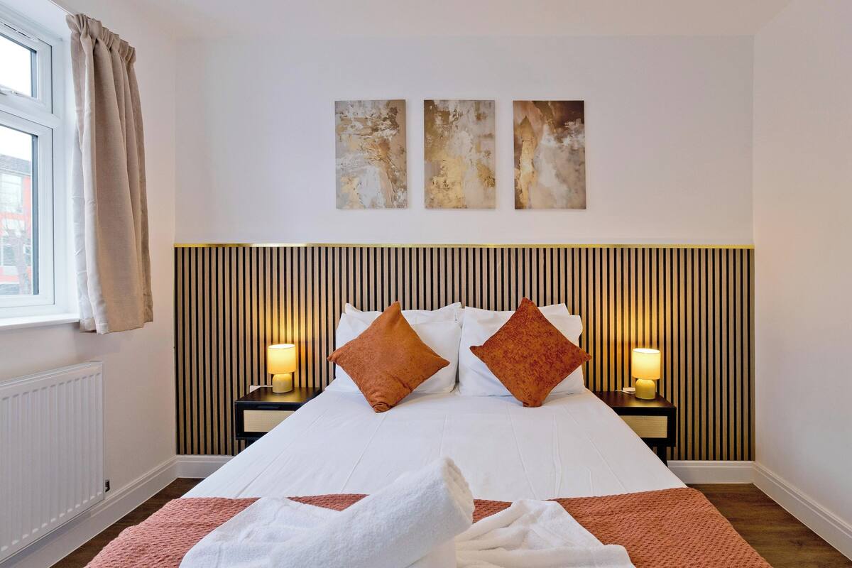 Une chambre d’hôtel avec un grand lit, deux lampes de chevet, un radiateur et une fenêtre avec des rideaux.