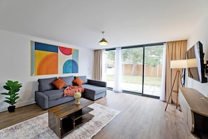 A modern living room with a grey sofa, a wooden coffee table, and a large abstract painting on the wall. - Imperial Woodberry Grove Apartments (London)